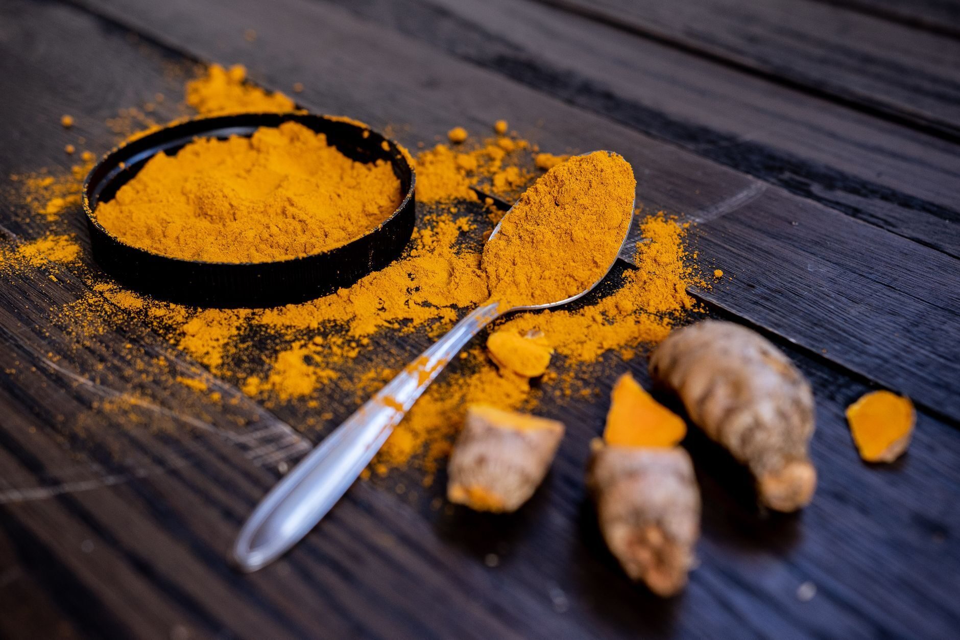 Golden turmeric powder and root on a dark wood surface